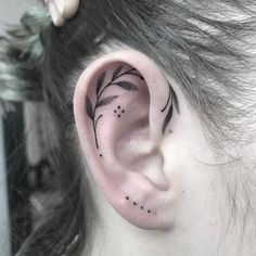 a woman's ear with black dots and leaves on her left behind the ear