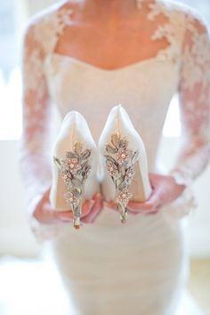 the bride is holding her wedding shoes in her hand and she is wearing a white dress with flowers on it