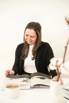 a woman sitting at a table with an open book and coffee in front of her