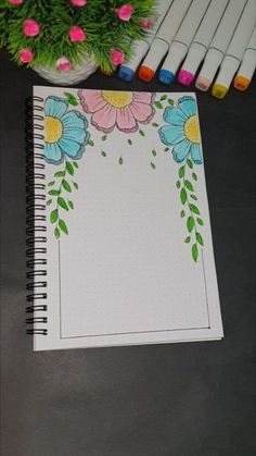 a notebook with flowers on it next to some crayon markers and a potted plant