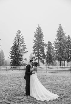 a bride and groom standing in the middle of a field with pine trees behind them