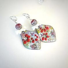 "These colorful artisan Lampwork bead and floral enamel earrings are comprised of 8mm artisan Lampwork glass beads done in a red base with ivory swirls and tiny white flowers. The gorgeous Lampwork beads are bottom capped with ornate Hill Tribe Silver bead caps and accented with white resin daisy spacer beads and Hill Tribe Silver beads. 33mm x 24mm enameled floral charms done in beautiful enamel bright green, pink, blue, and white with vibrant red flowers by artist Raida Disbrow dangle below the Lampwork beads. The earring component suspends from sterling silver lever back ear wires with a total length of 2.5\". These beautiful floral earrings are earrings you will enjoy for any occasion. Make a fabulous gift! Comes in a pretty gift box with fast shipping." Elegant Hand-painted Flower Earrings, Handmade Enamel Drop Flower Earrings, Handmade Enamel Flower Shaped Earrings, Elegant Nickel-free Enamel Flower Earrings, Whimsical Red Hand Painted Jewelry, Elegant Hand Painted Drop Flower Earrings, Elegant Red Hand Painted Jewelry, Hand Painted Red Elegant Earrings, Bohemian Flower Earrings As Gift