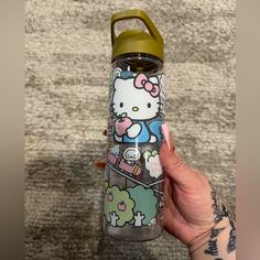 a person holding a hello kitty water bottle in front of a carpeted area with rugs