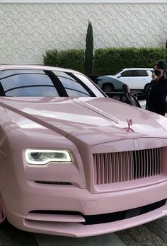 a pink rolls royce parked on the side of a road next to a man in a black jacket