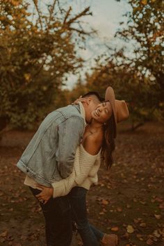 a man and woman are kissing in the park with autumn leaves on the ground behind them