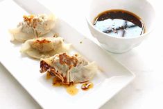 three dumplings on a white plate next to a bowl of sauce and a spoon