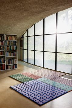 an empty room with several bookshelves and rugs on the floor in front of large windows