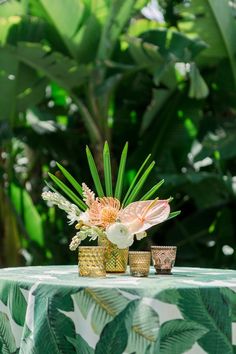 an arrangement of flowers in vases on a green table cloth with palm leaves around it