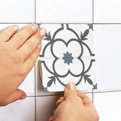 two hands are using a tile stencil to decorate a flower design on a wall