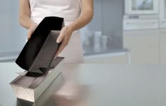 a woman is holding a black box on top of a silver table in the kitchen