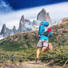 a man is running on a trail in the mountains with snow capped peaks behind him