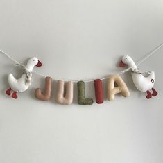 the name julia spelled with felt ducks hanging on a string in front of a white wall