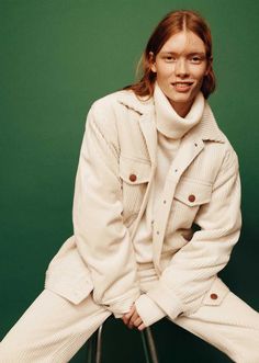 a woman sitting on top of a stool wearing white clothing and boots with her hands in her pockets