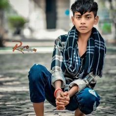 a young boy sitting on the ground with his hands in his pockets and wearing a scarf around his neck