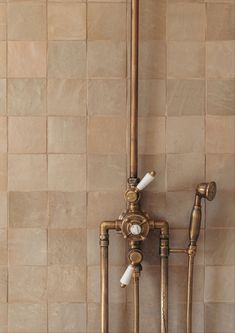 an old fashioned faucet in the corner of a tiled wall with pipes attached to it