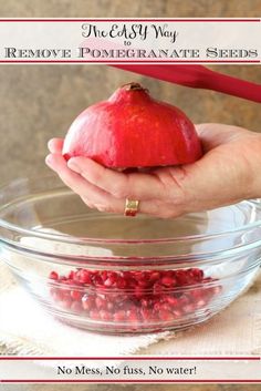 a hand holding an apple over a bowl filled with pomegranates