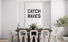 a dining room table with white chairs and a poster on the wall above it that says catch waves