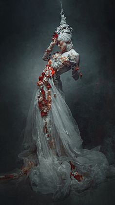 a woman in a white dress with red flowers on her head and arms, standing against a dark background