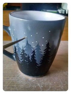 a cup with trees painted on it and a pair of scissors sticking out the side