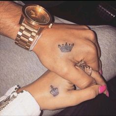 two people holding hands with tattoos on their fingers and wristbands, both wearing crowns