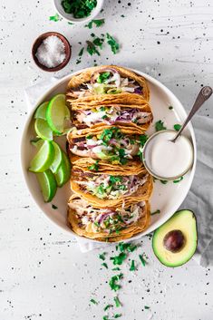 a white plate topped with tacos and guacamole next to an avocado