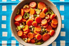 a bowl filled with carrots and green peppers on top of a blue table cloth