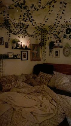 an unmade bed in a room with many pictures on the wall and hanging plants