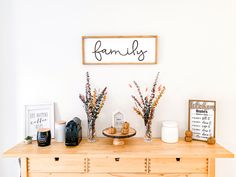 a wooden table topped with two vases filled with flowers next to a sign that says family