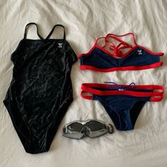 two swimsuits and sunglasses are laid out on a white sheet with a pair of swimming goggles