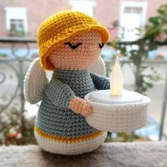 a crocheted doll holding a lit candle on top of a table next to a window