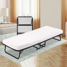 a bed sitting on top of a hard wood floor next to a white couch and chair