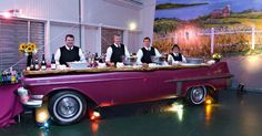 a group of men sitting at a table in front of a purple car with food on it