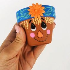 a hand holding up a clay toy with a flower on it's head and eyes