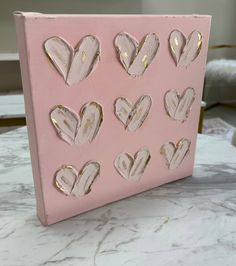 a pink and gold painted canvas with hearts on it sitting on a marble countertop