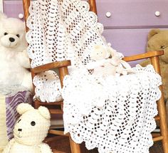 two teddy bears sitting next to a crocheted baby blanket on a rocking chair