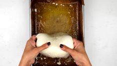 two hands holding a loaf of bread on top of a baking sheet with icing