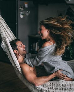 a man and woman are laying in a hammock together, smiling at each other