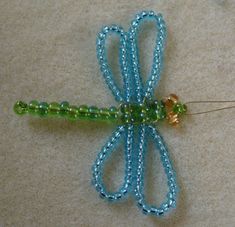 a blue and green beaded dragon brooch sitting on top of a white surface