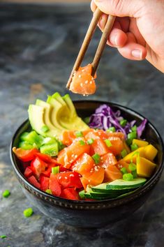 someone is holding chopsticks over a bowl of food with vegetables and avocado