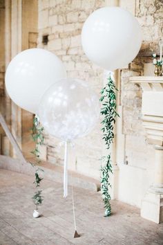 two white balloons with greenery tied to them in front of an old brick wall