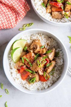 two white bowls filled with chicken and rice on top of a table next to a fork