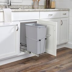 a kitchen with white cabinets and wood flooring has a pull out trash can in the middle