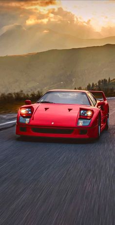 two red sports cars driving down the road in front of a mountain range at sunset