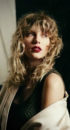 a woman with blonde hair and red lipstick posing for a photo in front of a window