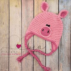 a pink crocheted pig hat on top of a wooden surface with the word love written across it