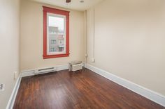 an empty room with hard wood flooring and red window