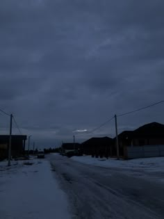 an empty street with snow on the ground and power lines in the distance at night