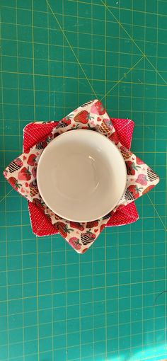 a white bowl sitting on top of a red and green placemat next to a cutting board