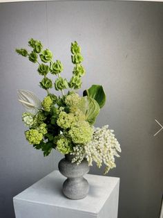 a vase filled with lots of green flowers on top of a white pedestal next to a wall