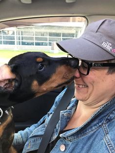 a woman is kissing a dog in the back seat of a car while wearing glasses and a hat